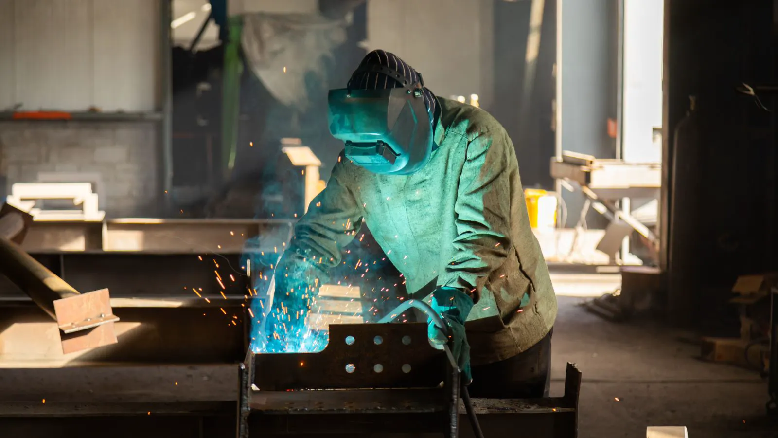 Welder wearing face shield and heavy gloves near an arc