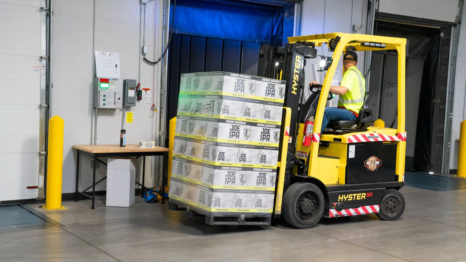 Forklift forks lifting a standard wooden pallet in a warehouse