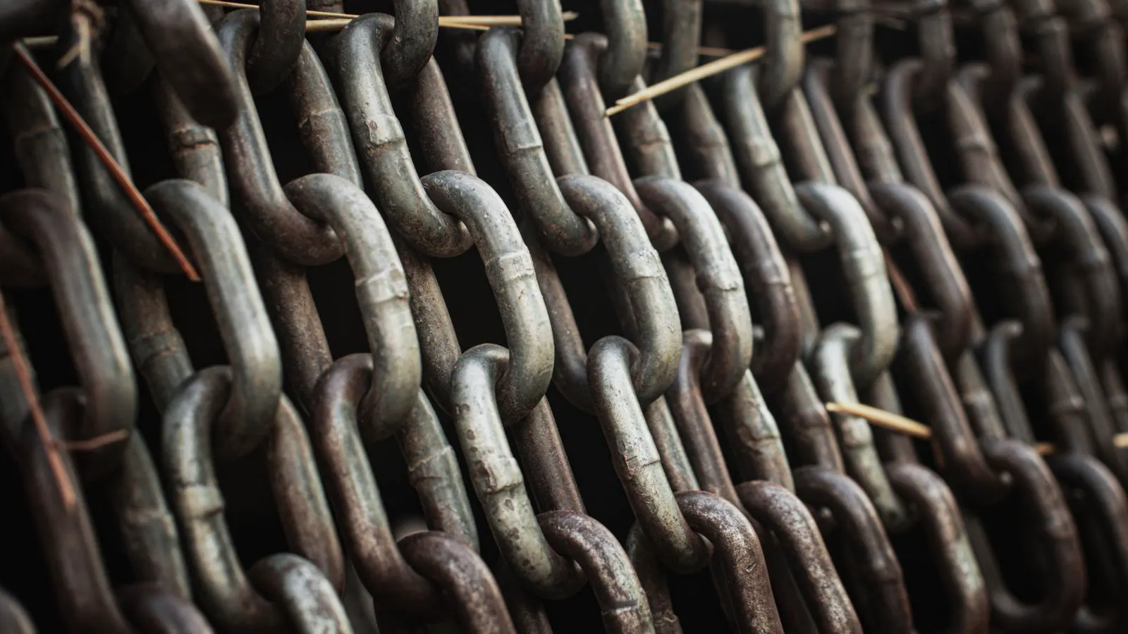 A thick chain sling hanging vertically from a crane hook, supporting a heavy steel load.