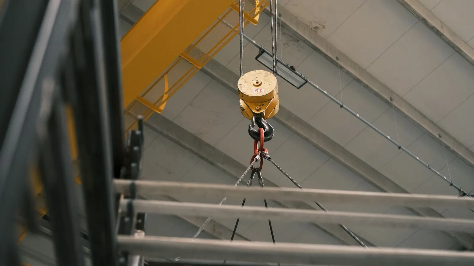 A steel bridge crane suspended over a factory floor with a hook block hanging.