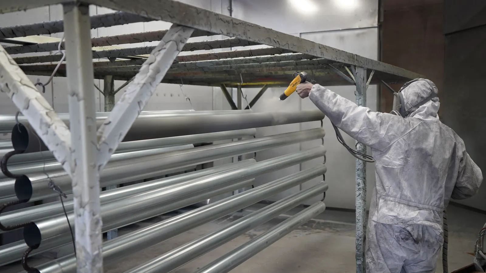 A metal part moves through a powder coating booth in a factory.