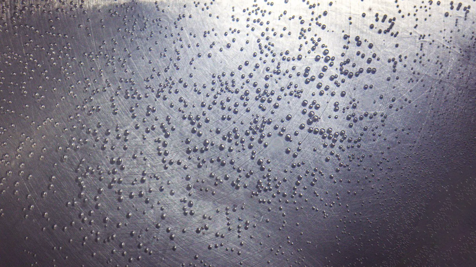 Metal component positioned near a blasting nozzle during surface preparation.