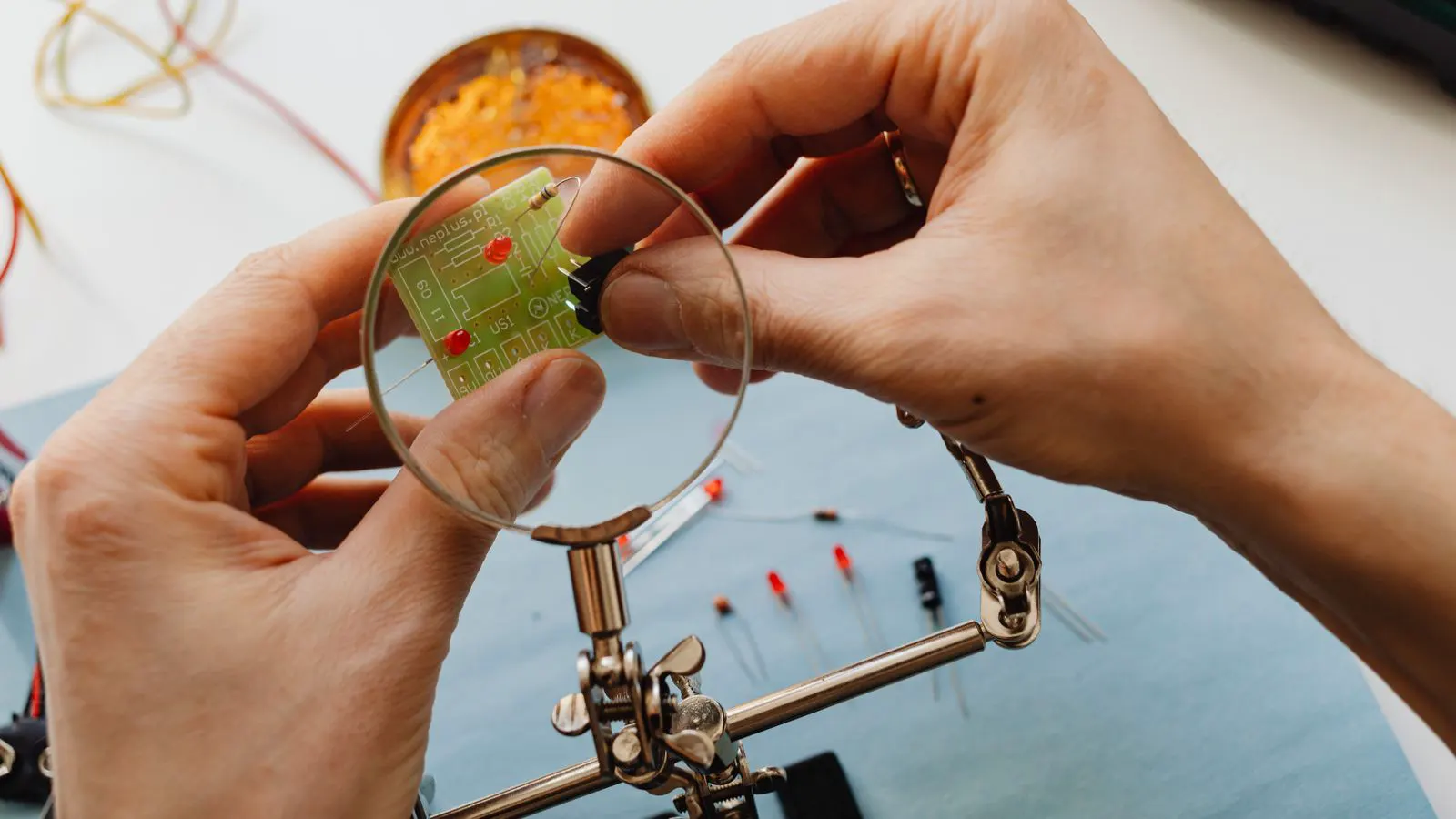 A technician holding a component under a magnifying lamp