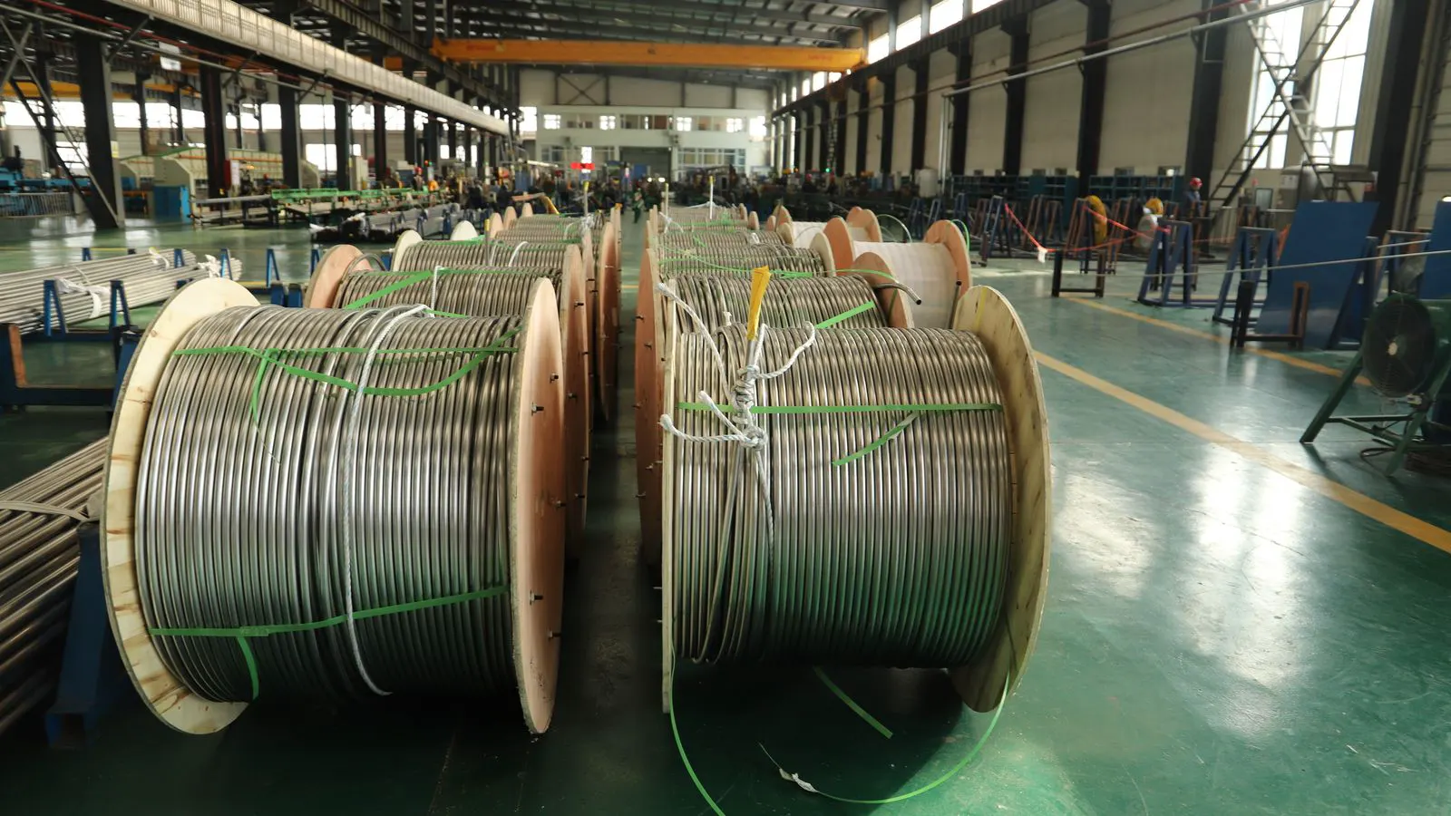 Industrial workers inspecting large spools of copper wire in a plant.