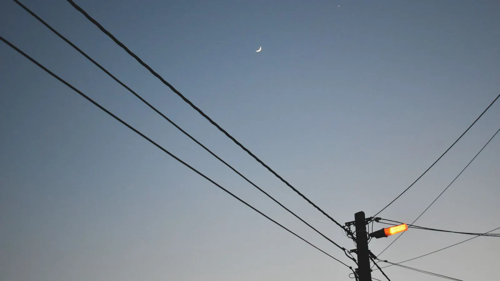 A modern street light pole standing against a dark blue evening sky.