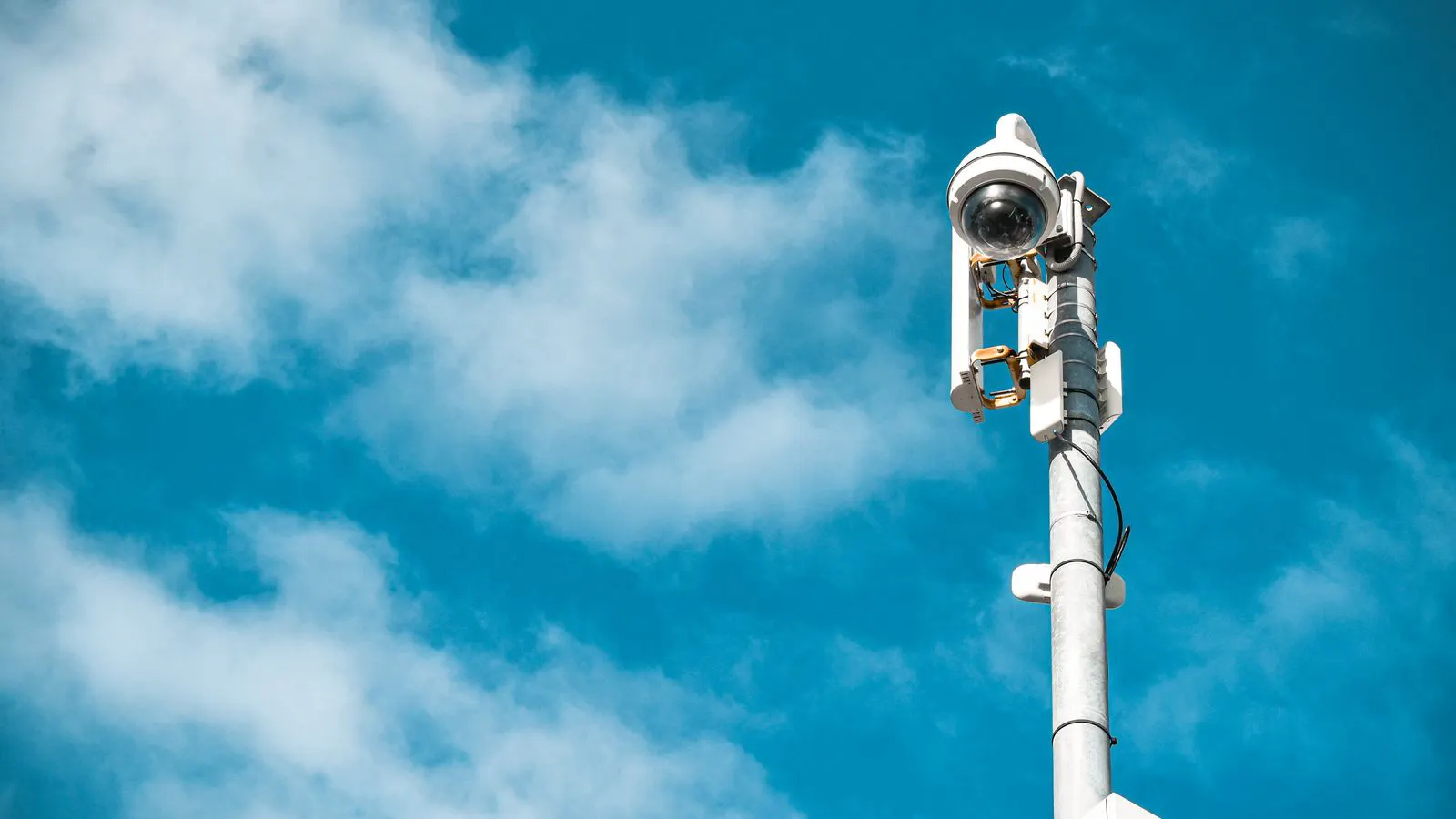 A white dome camera mounted on a metal pole in a rural area