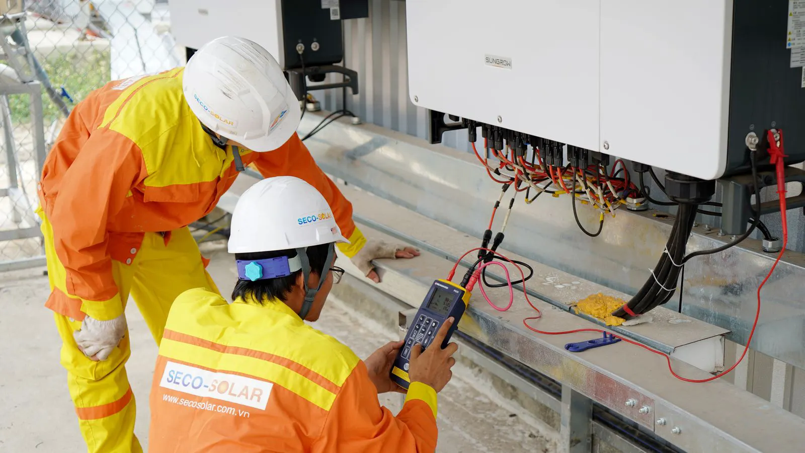 Workers installing solar tracker rails on a prepared concrete pad.