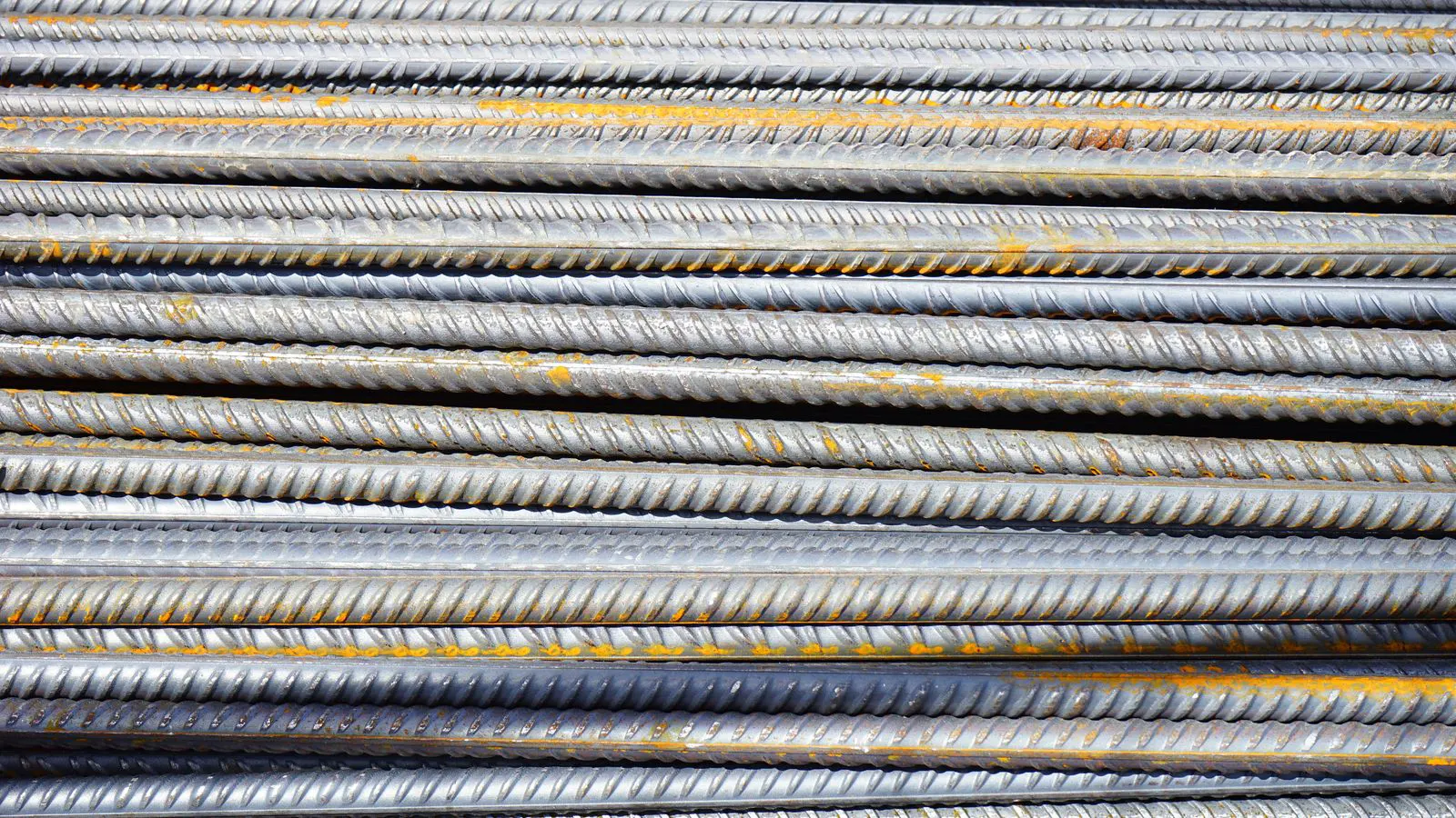 A worker inspecting a stack of steel round bars with a tape measure.