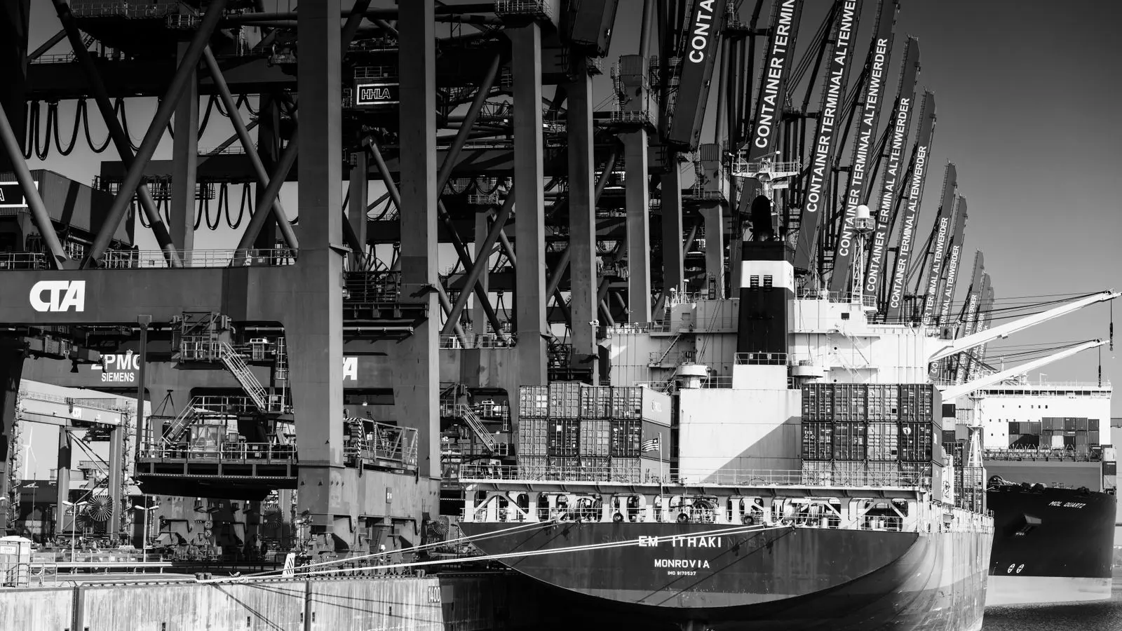 A large container ship docked at a busy port terminal.