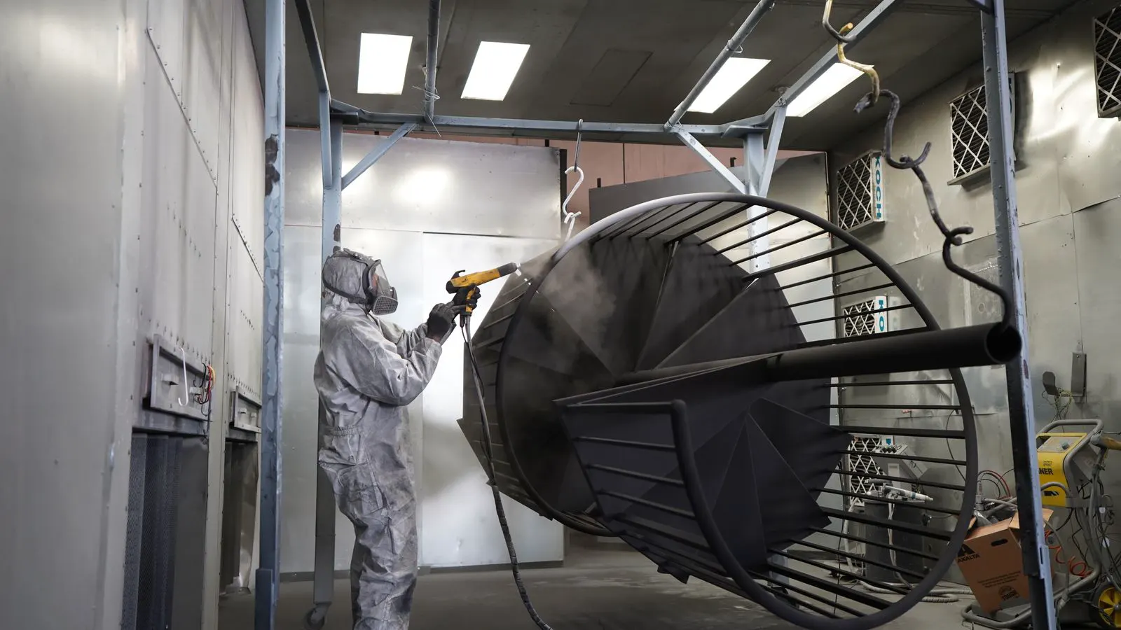 Inside of a large industrial powder coating booth with hanging racks