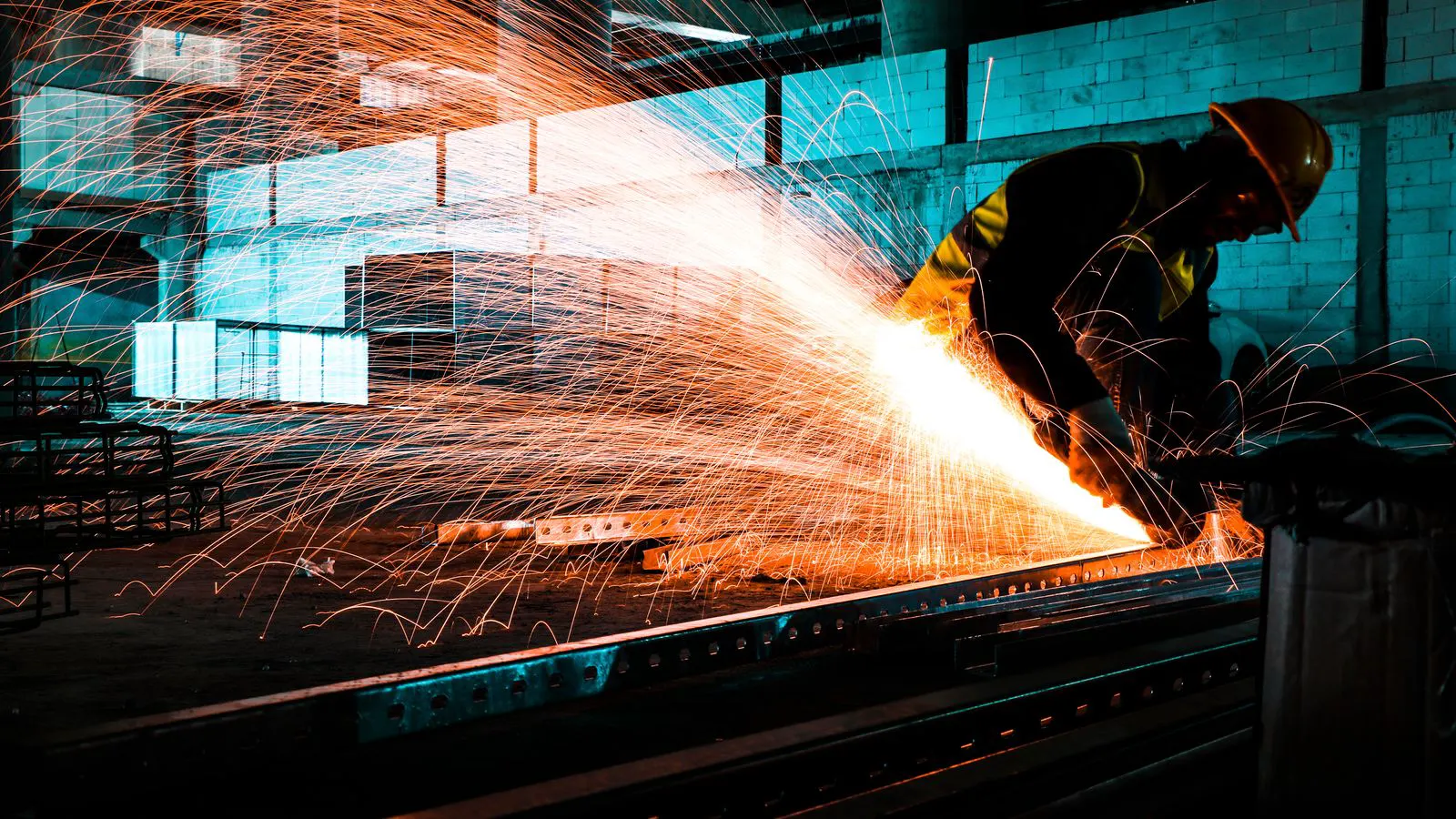 A worker wearing protective gear cuts a steel container wall.