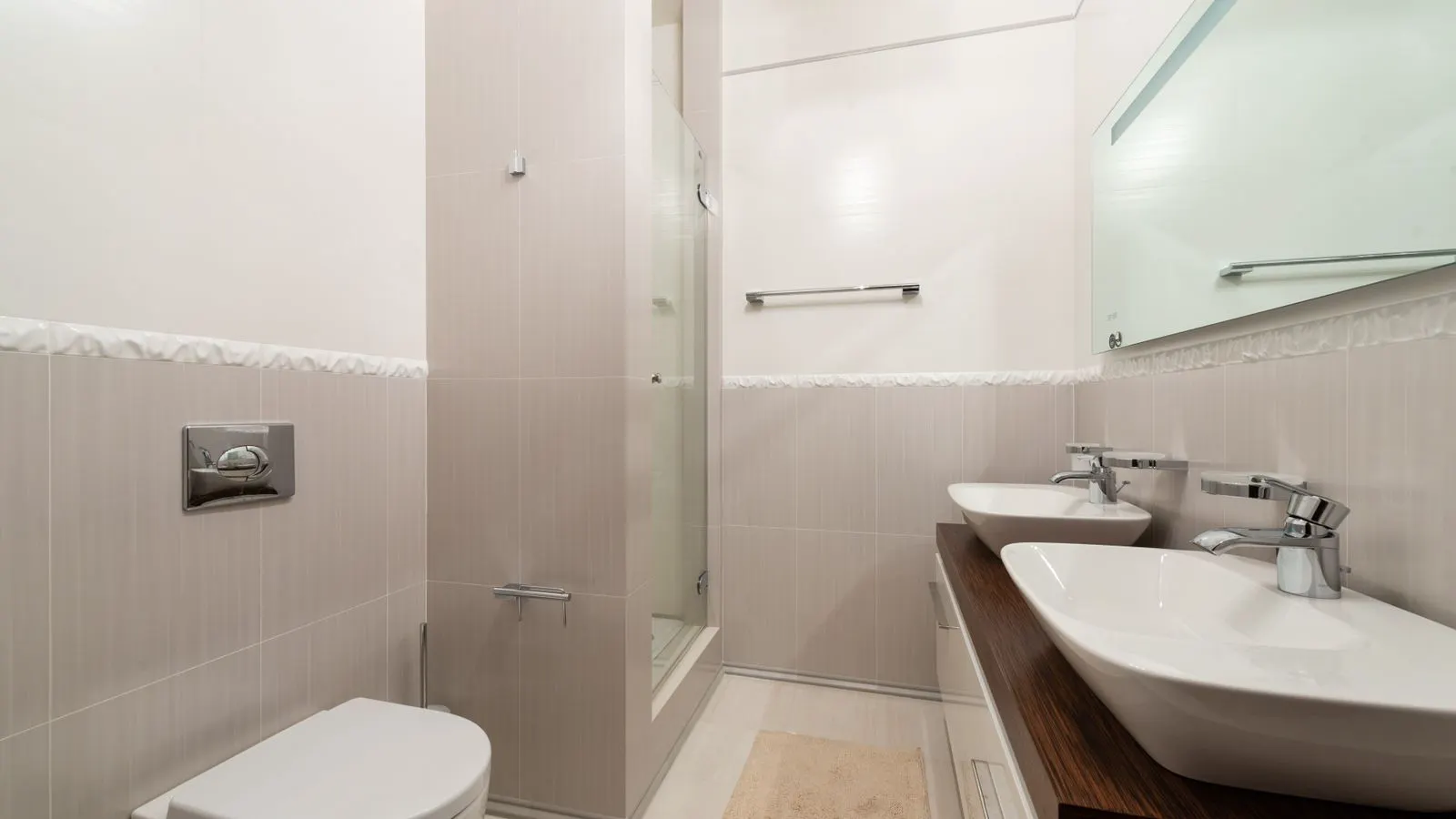 A white monobloc toilet next to a two-piece toilet in a tiled room.