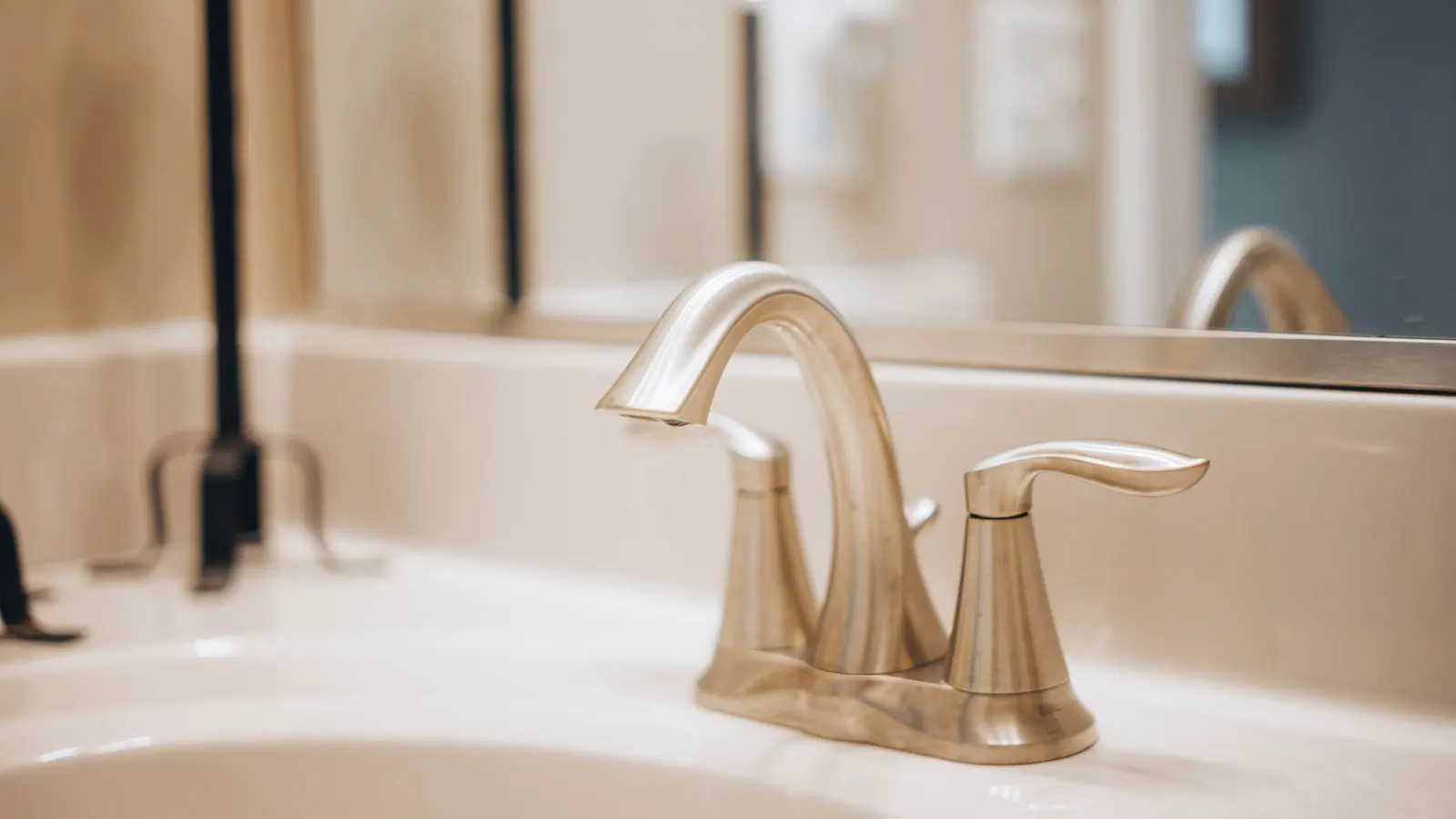 A close up of a bathroom faucet handle with visible water droplets forming on the spout tip.