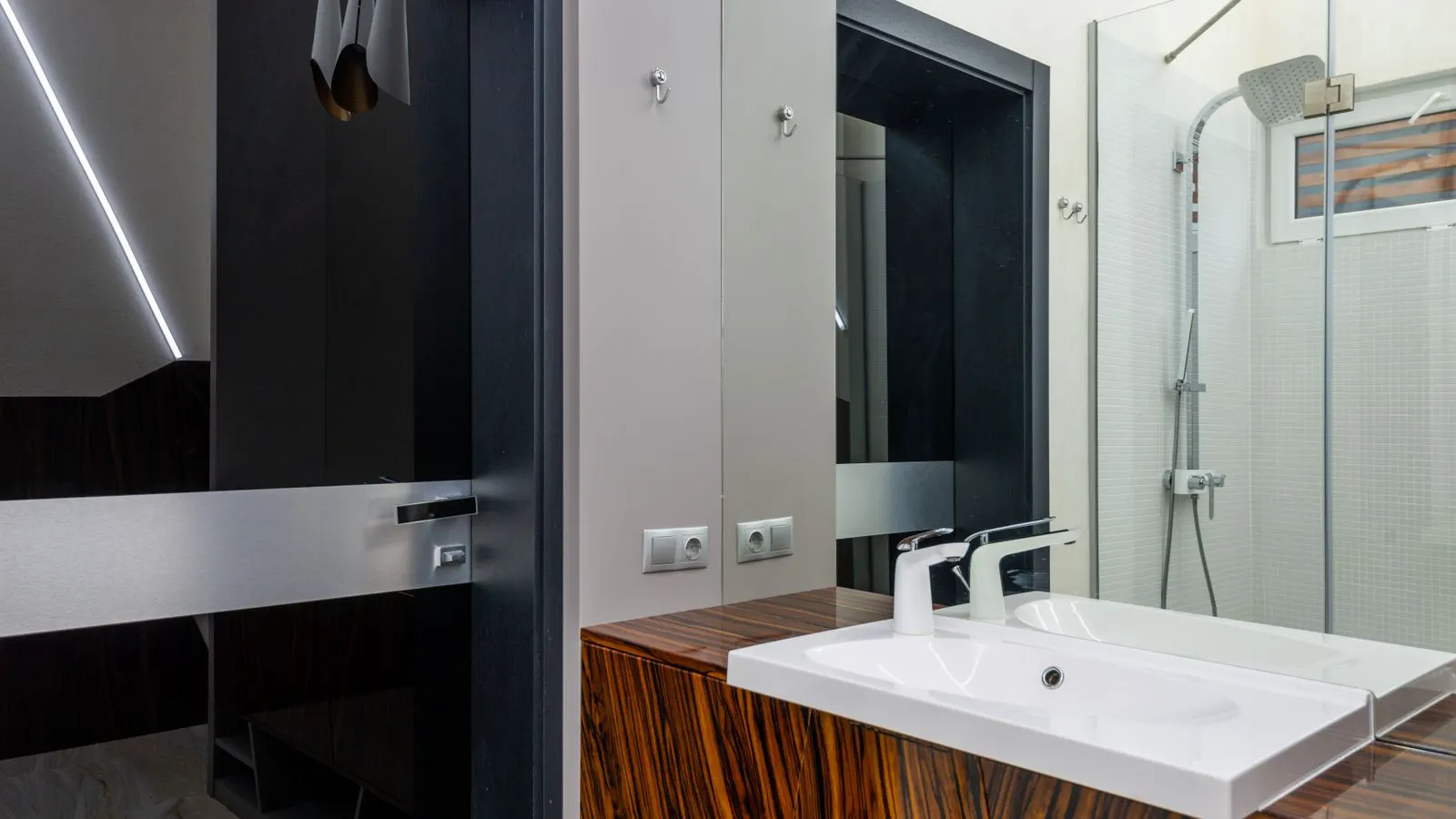 A modern white ceramic toilet sits beside a chrome shower mixer valve in a bright bathroom.