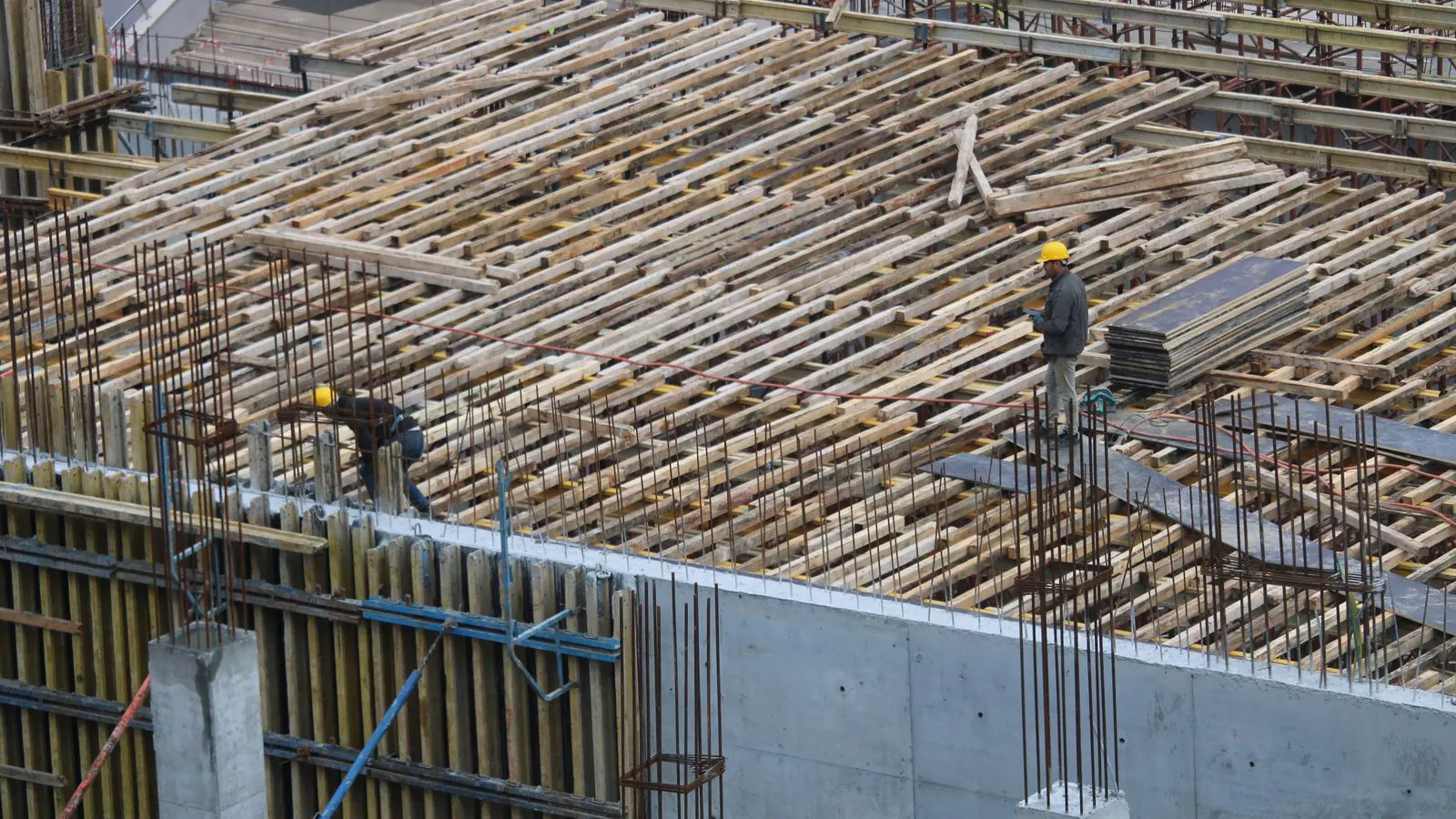 Workers inspecting stacked aluminum formwork panels on a delivery site