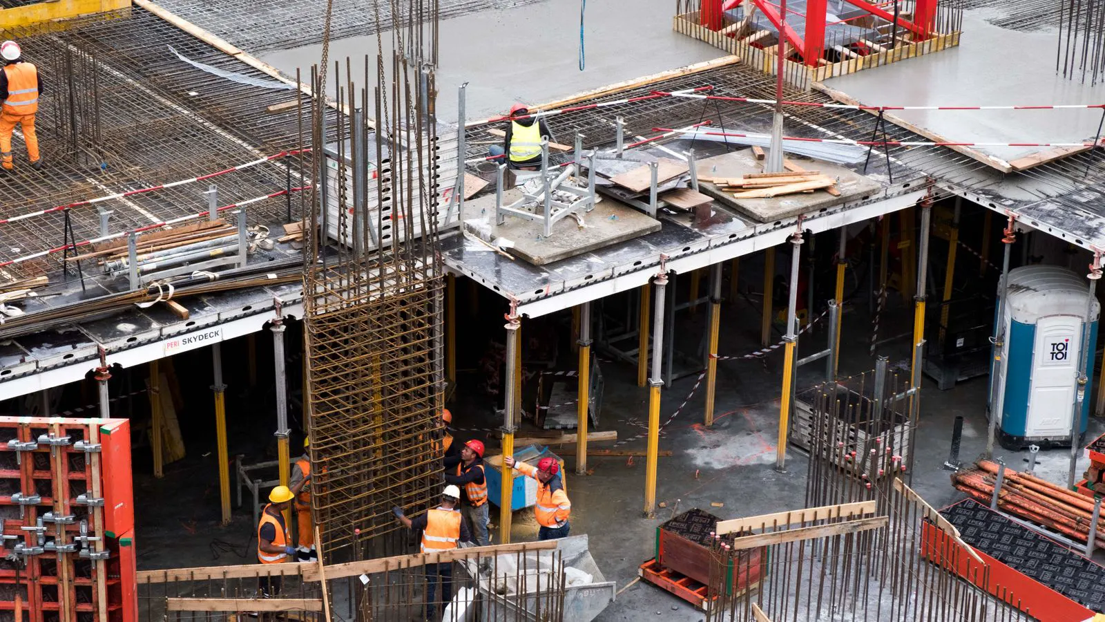 Workers inspecting vertical steel shoring props in a concrete formwork area.