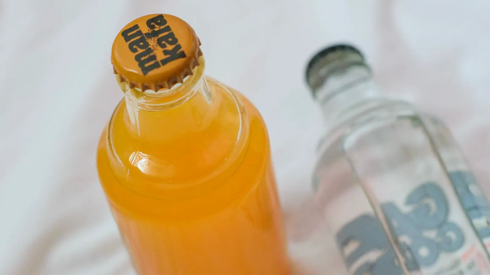 A clear glass bottle and a transparent PET bottle side by side on a table.