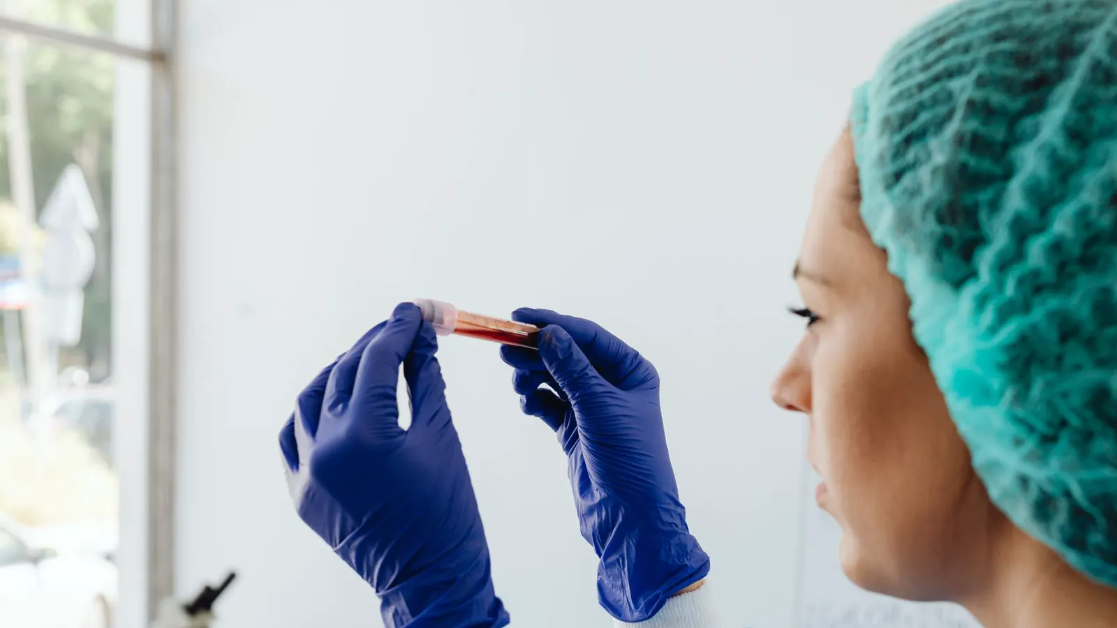 A laboratory technician holds a rectangular nonwoven fabric sample near a testing machine.