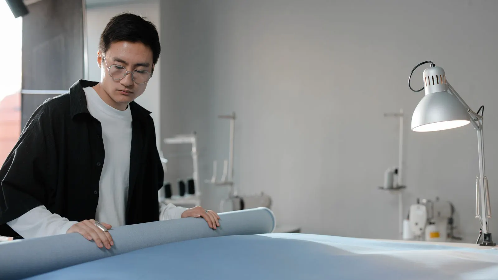 An inspector holds a measuring tape against a roll of white nonwoven fabric.