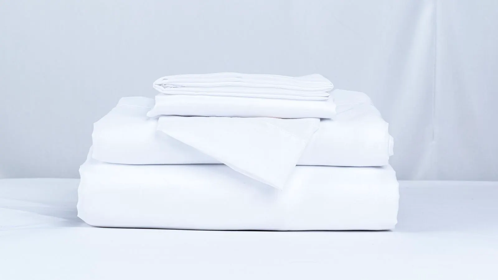 Neatly stacked white hotel bedding sheets on a wooden table