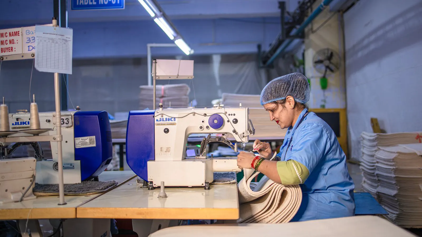 A sewing machine needle threading through layered fabric in a factory setting