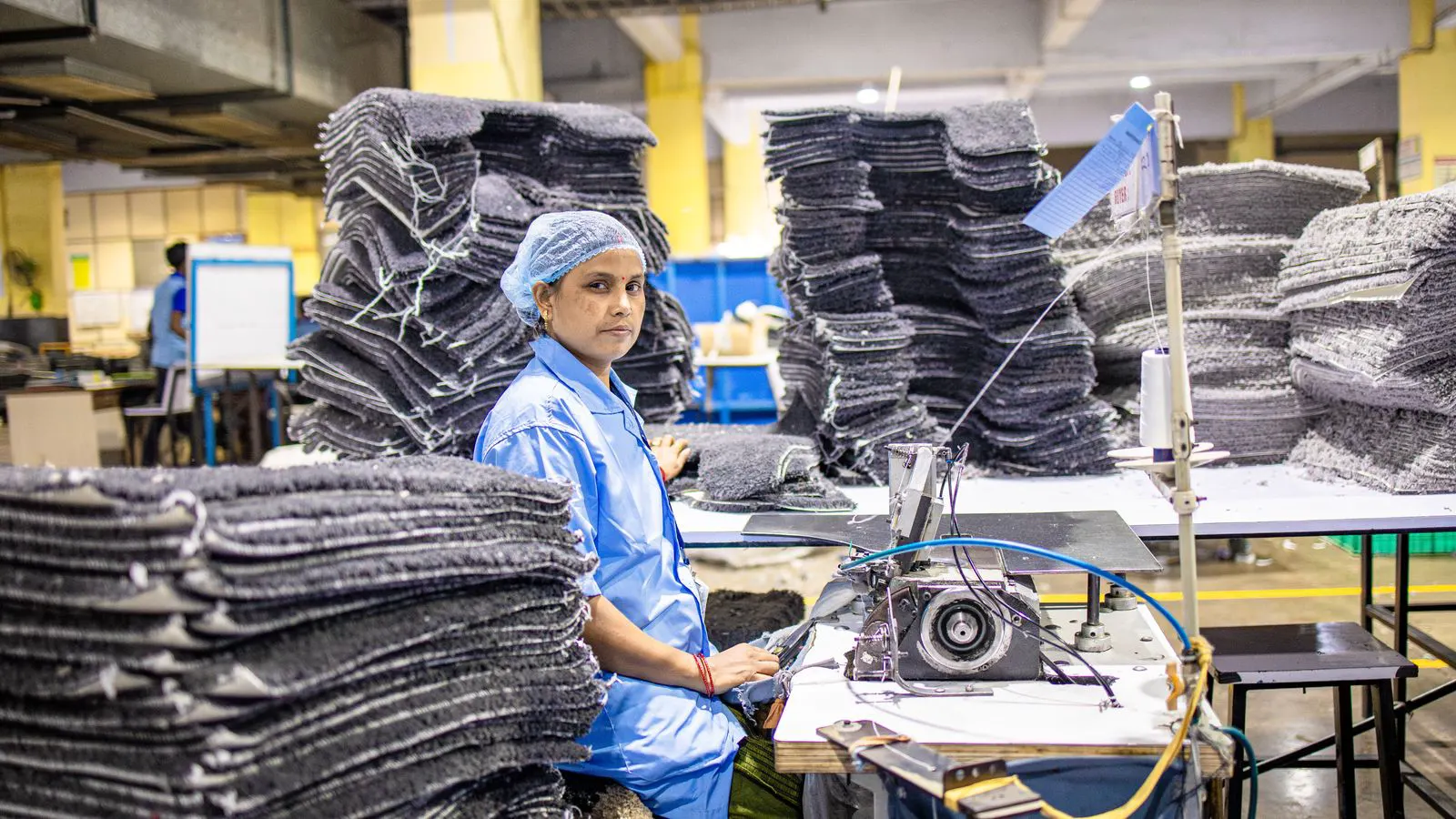 A worker operates a heavy industrial sewing machine in a bag factory.