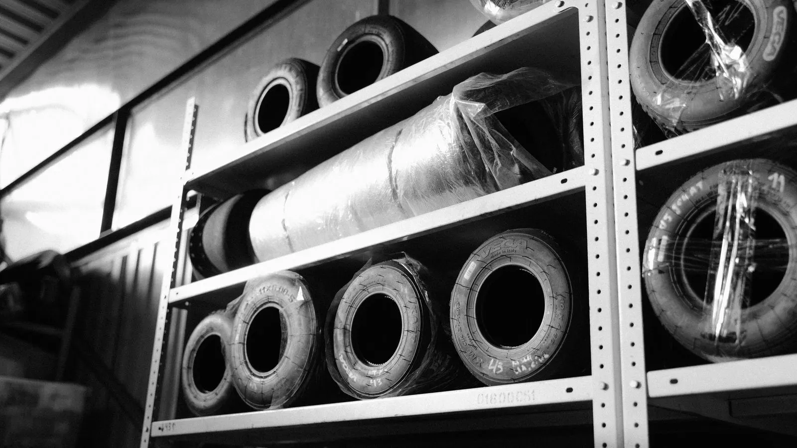 A row of new tires stacked on a wooden rack inside a warehouse.