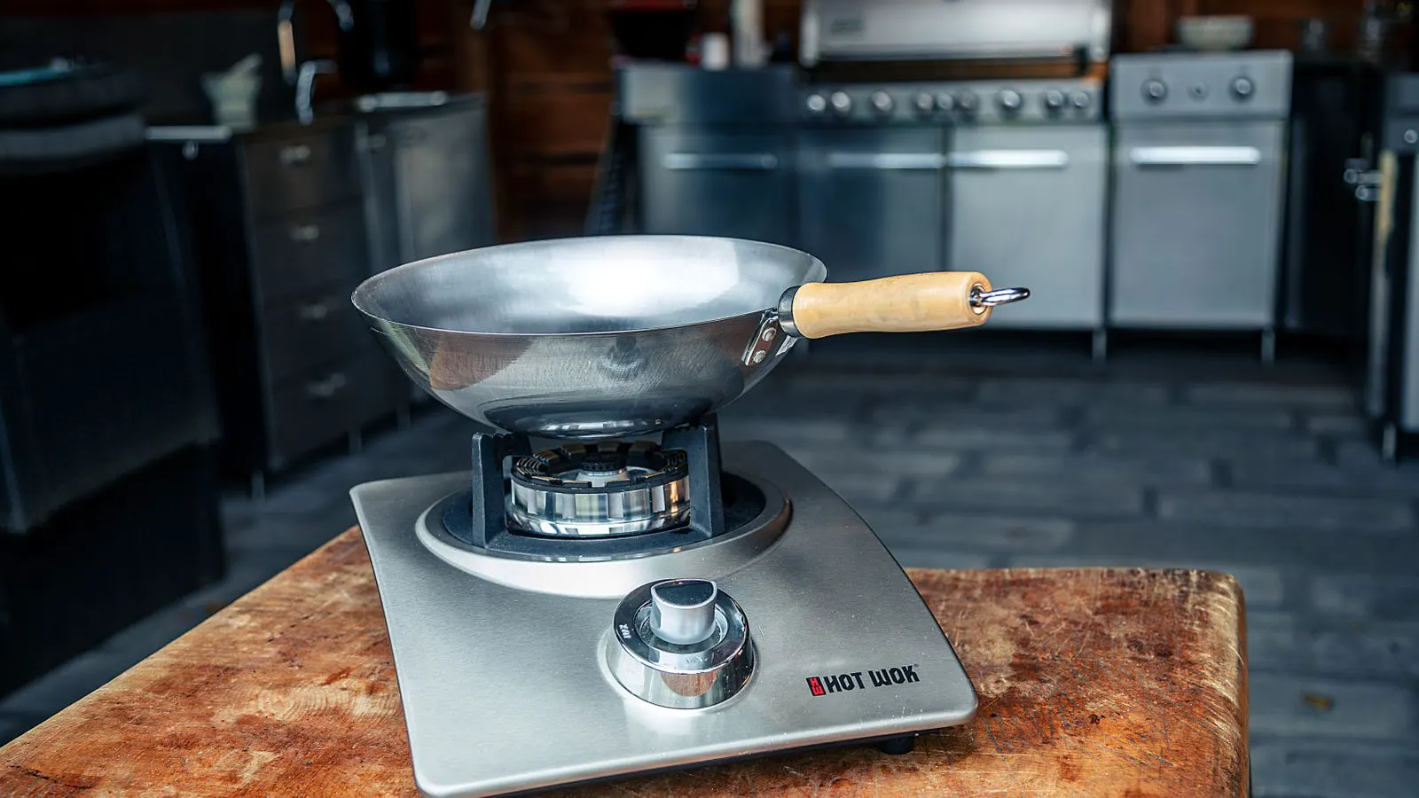 A stainless steel wok with a flat base resting on a workbench.