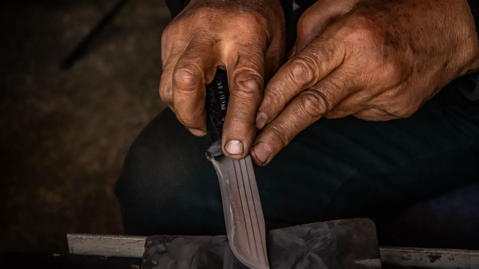 A pair of hands holding a chef knife against a flat whetstone for sharpening