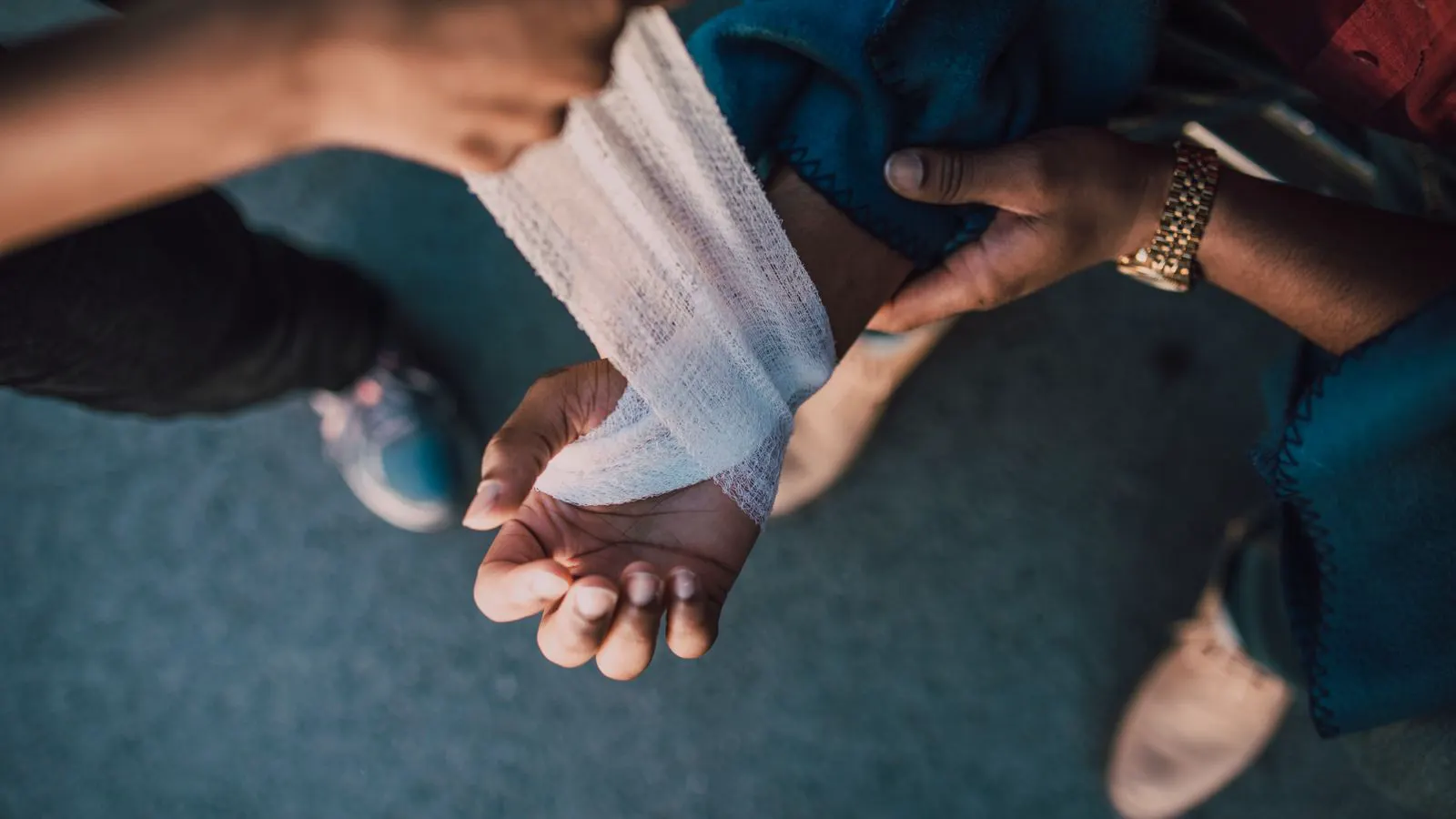 A pair of hands applying a small adhesive bandage to a wound.