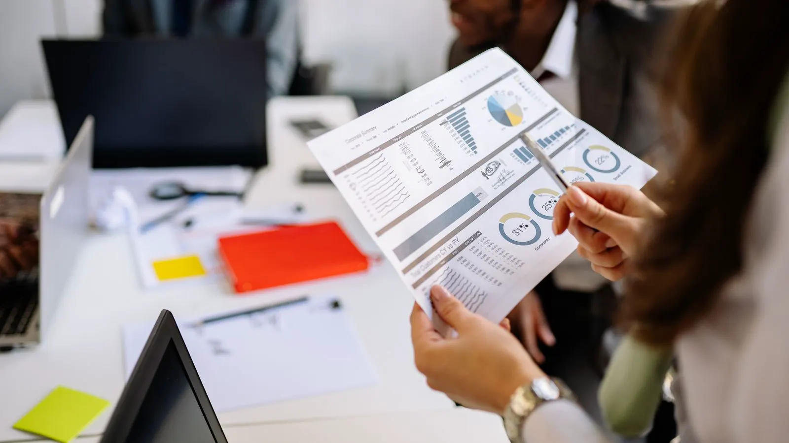 Two professionals comparing printed cost comparison documents at a desk.