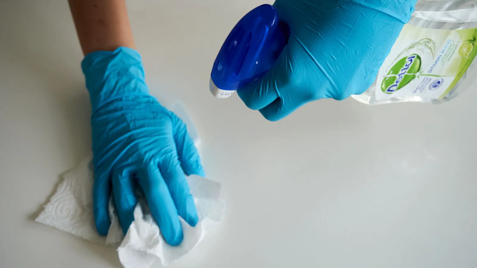 Two gloved hands wiping a work surface with a white lint-free cloth