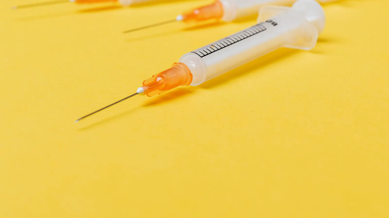 A row of sterile syringes and needles on a clinical surface