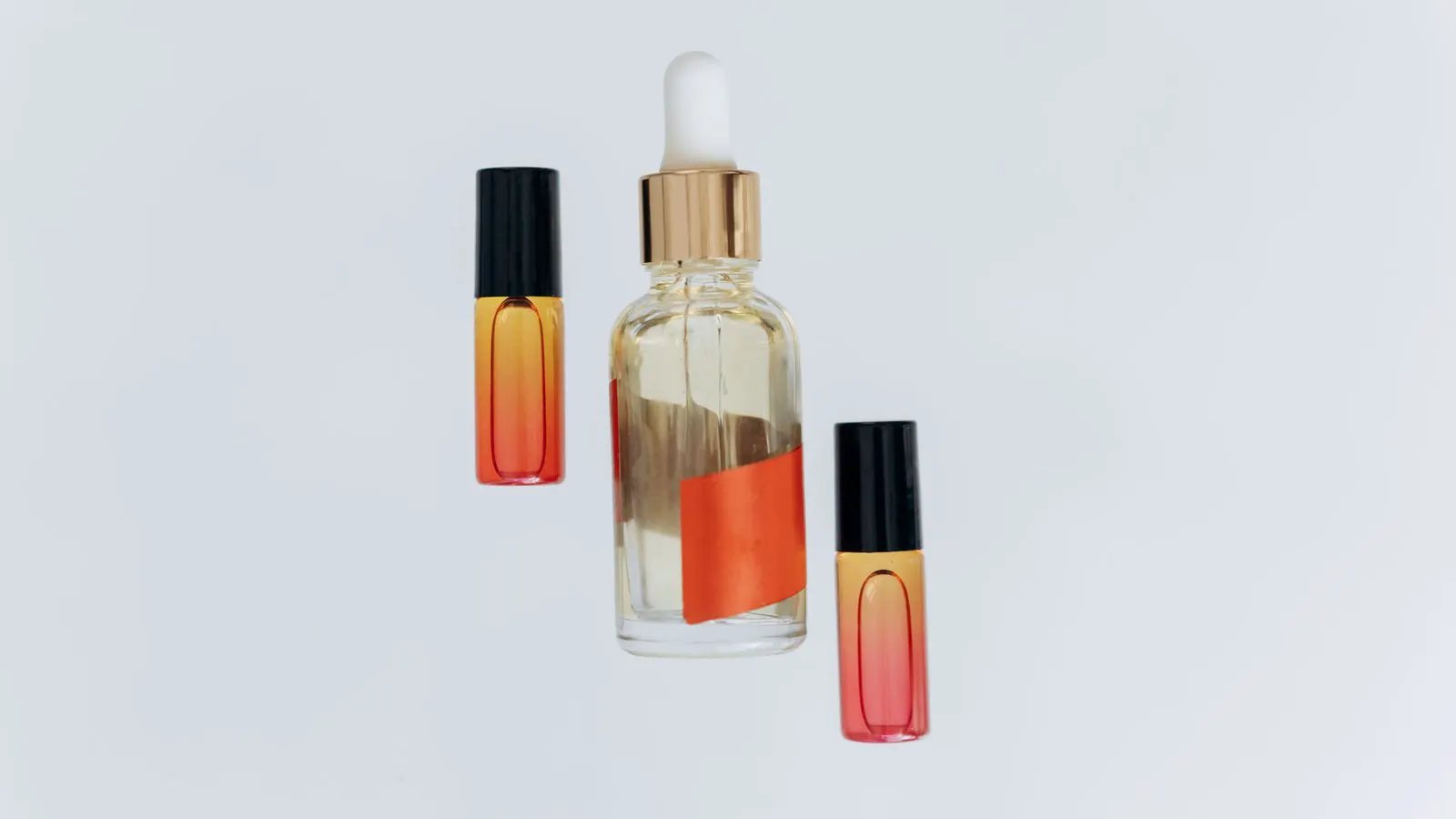 Three cosmetic bottles made of glass, plastic, and metal sit side by side