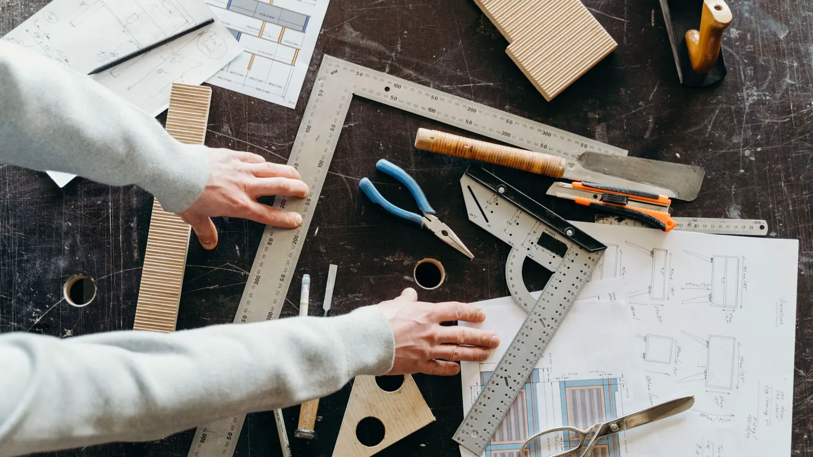 A blueprint and cost table on a workbench next to a woodworking machine.