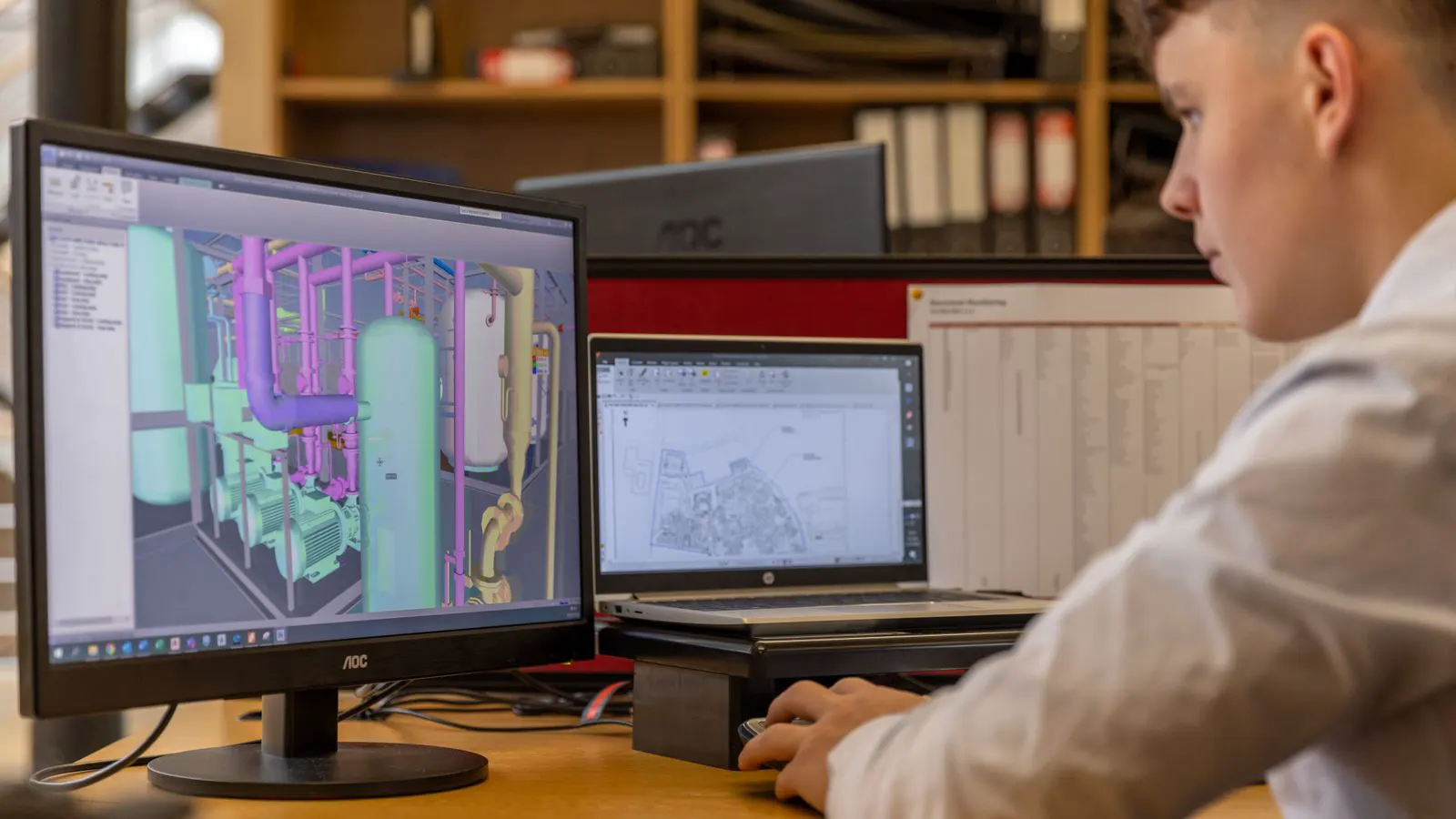 Two professionals examining a machining drawing on a desktop monitor