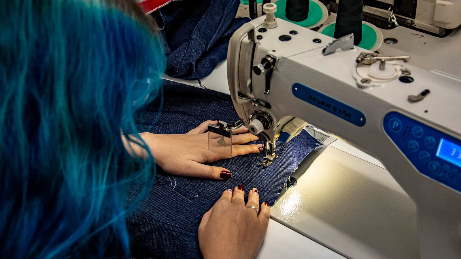 A close view of a presser foot clamped to a heavy denim fabric sample on a sewing machine.