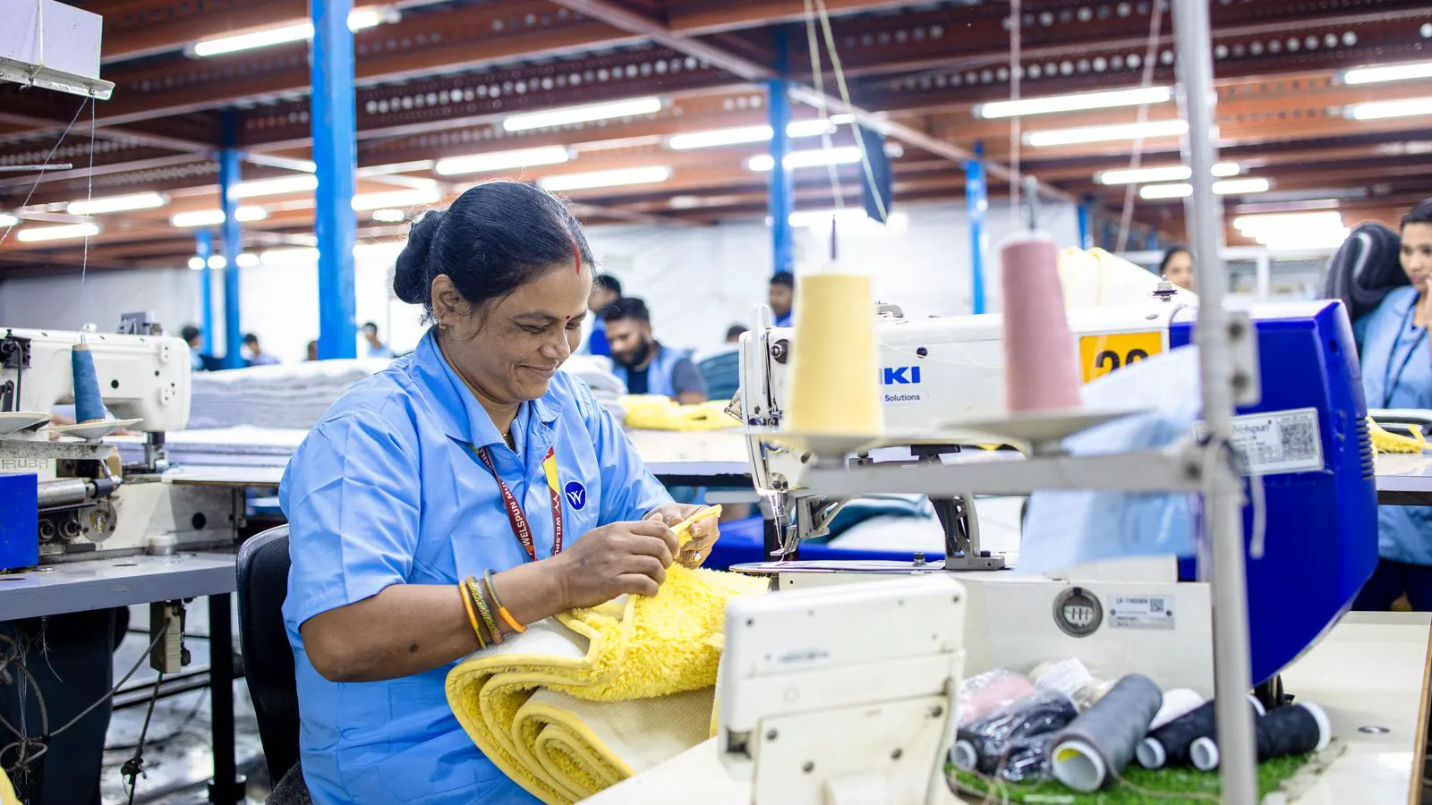 A robotic arm suspended above a garment sewing line in a factory.