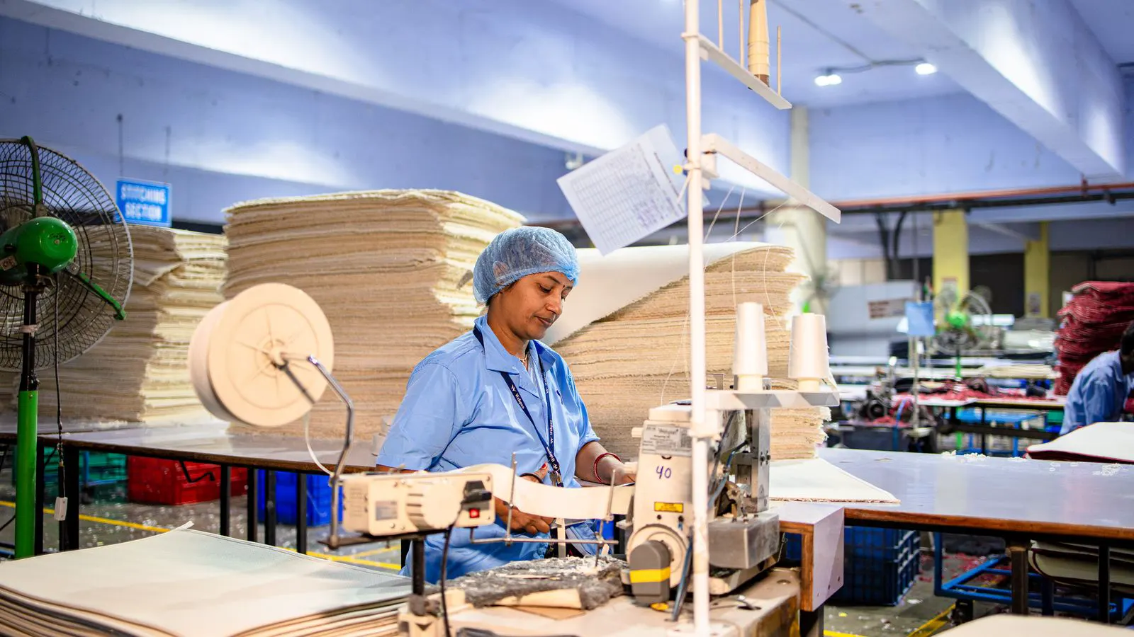 A modern industrial sewing machine on a clean factory floor with an operator nearby.