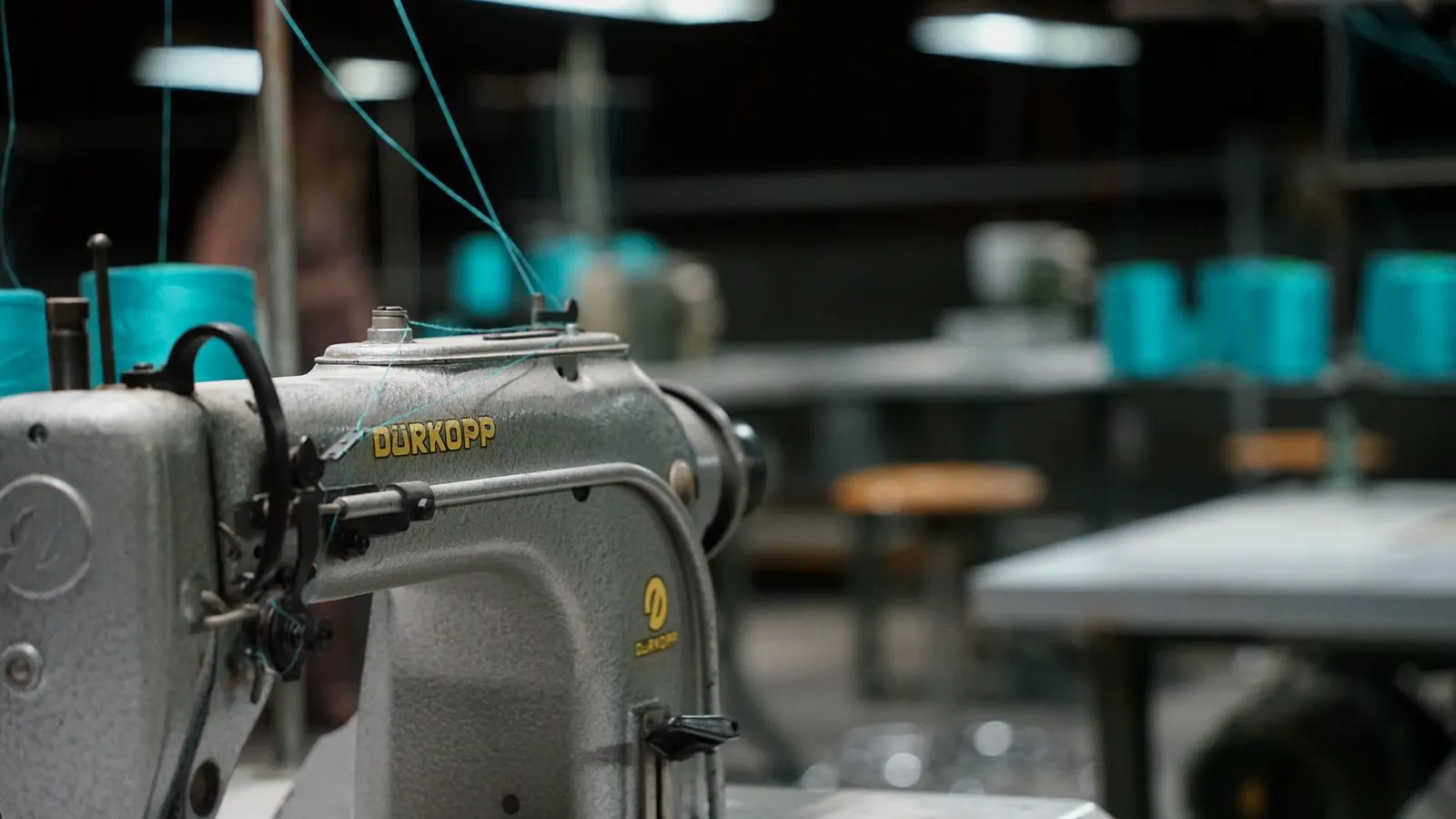 Close view of thread tension dial and feed mechanism on an industrial sewing machine.