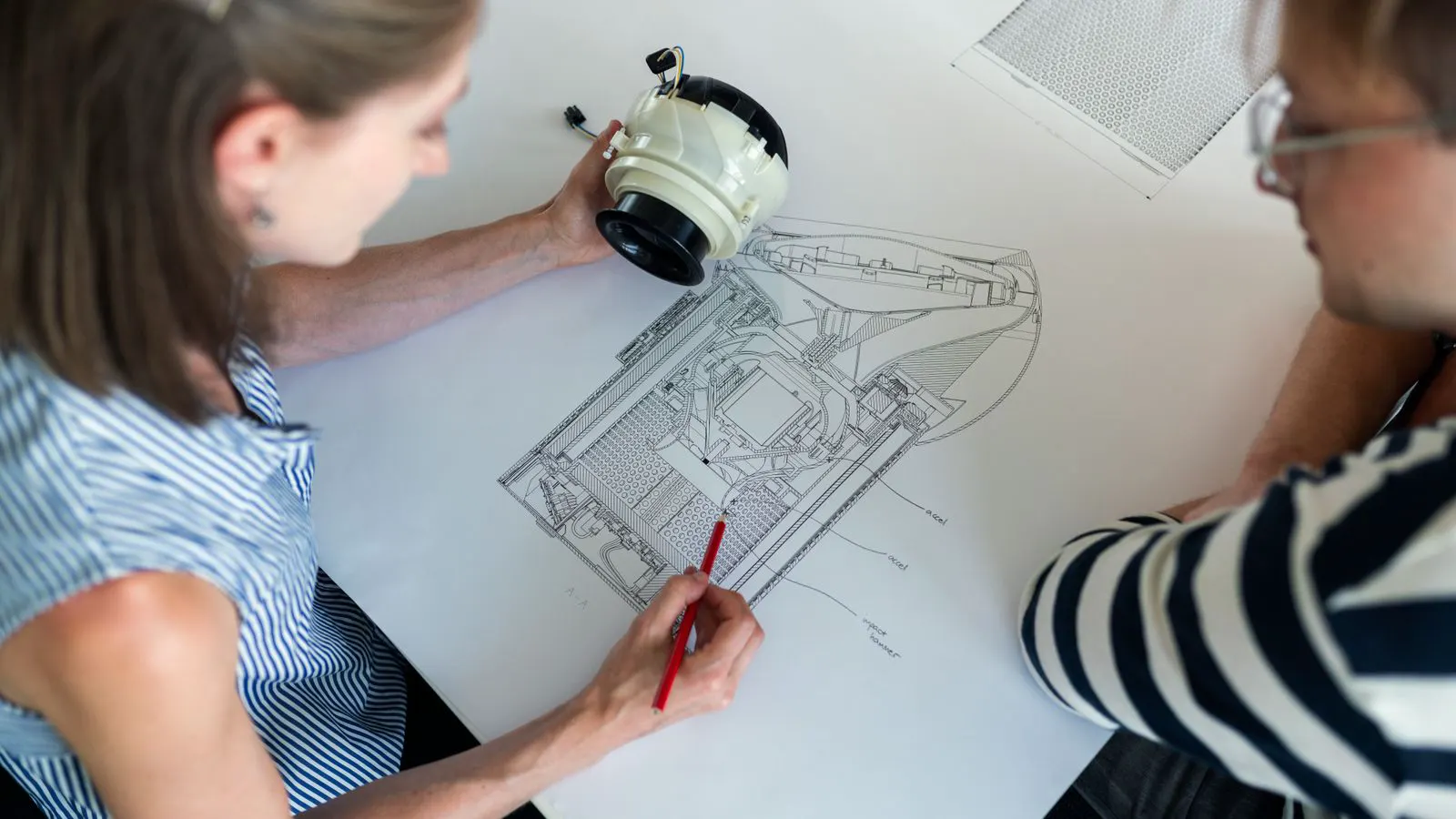 A detailed engineering drawing of a bent sheet metal bracket on a desk.