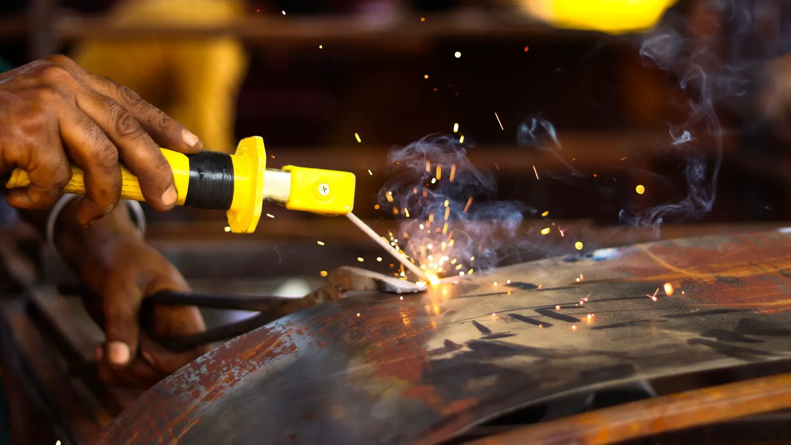 A worker using a welding torch on a sheet metal panel