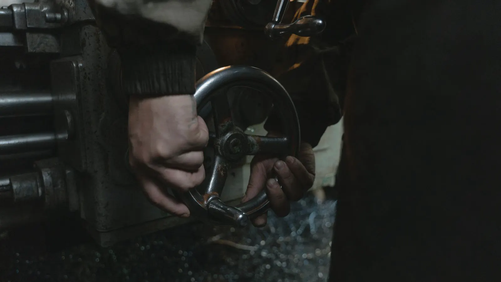 A machinist holding a forged steel part under a bright inspection light.