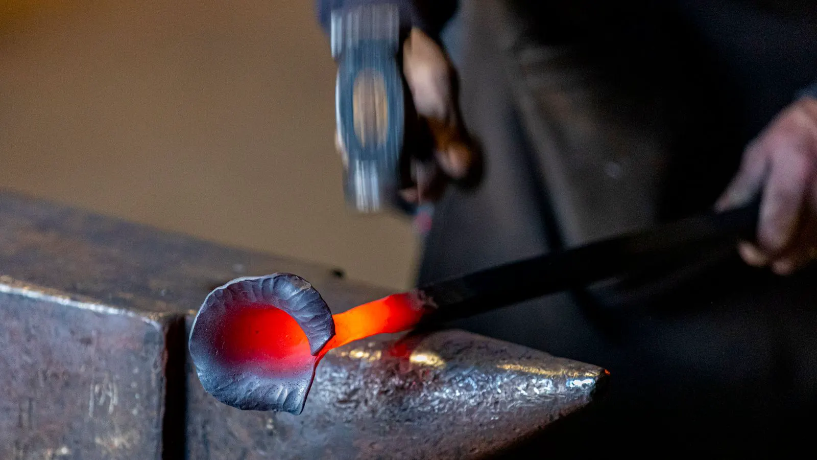 Industrial forging hammer striking a glowing metal billet on a die bed