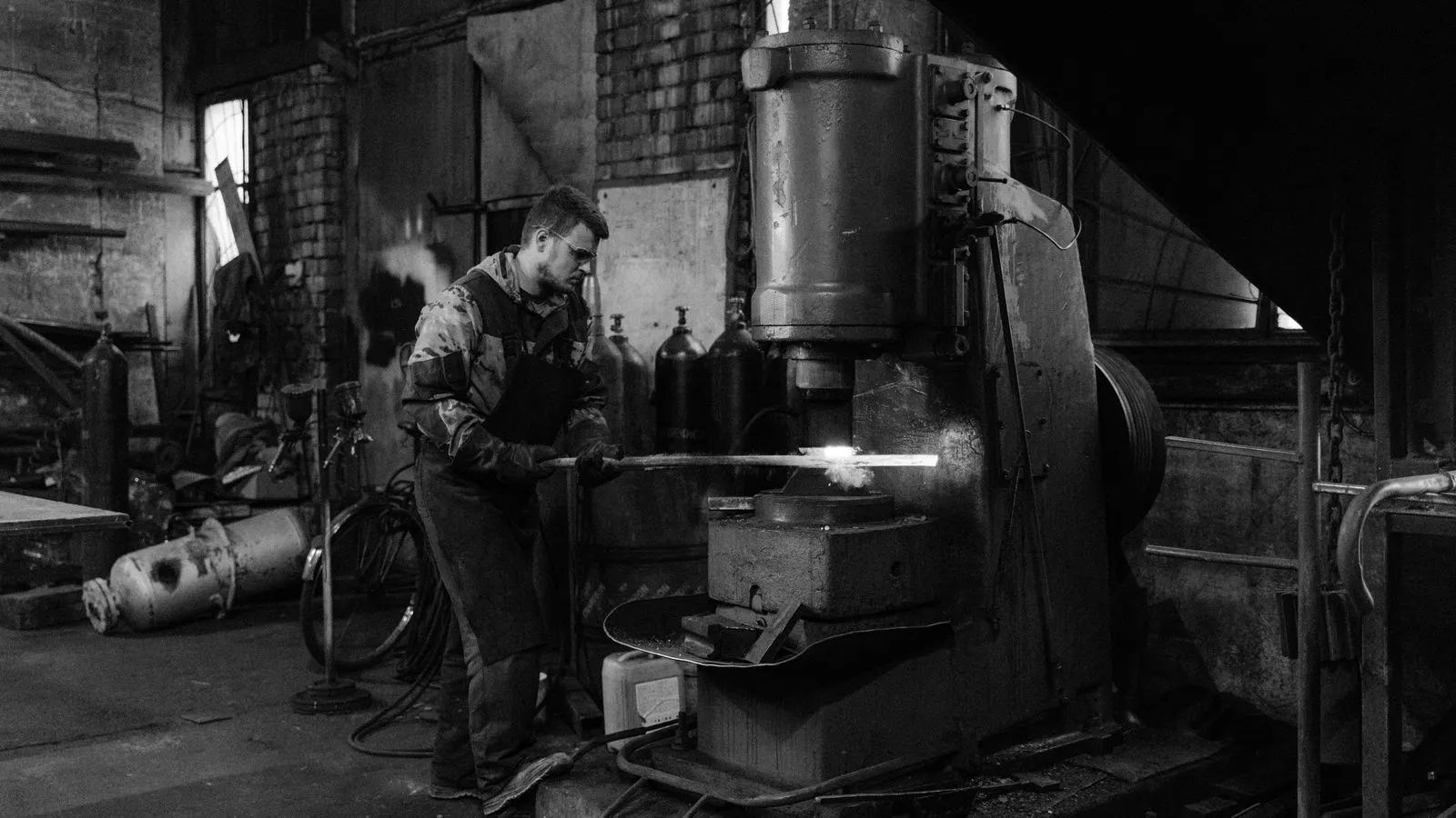 A heavy hammer compresses a hot metal billet on a forging anvil.