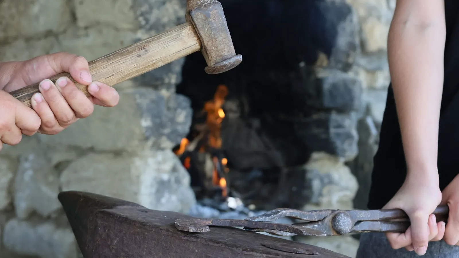 A large hammer compresses a hot billet of metal on an anvil.